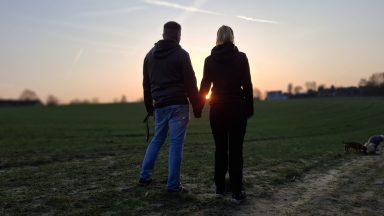 Paar hält Händchen bei Sonnenuntergang auf einem Feld.