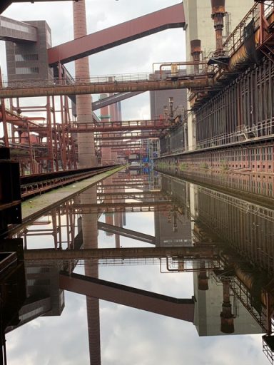 Stahlwerk mit reflektierendem Wasser und industriellen Strukturen im Hintergrund.
